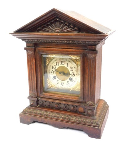 A late 19thC German oak cased mantel clock, the brass square dial with foliate spandrels, circular silvered chapter ring bearing Arabic numerals, Junghans eight day movement with coil strike, the case of carved architectural form, with pendulum and key, 3