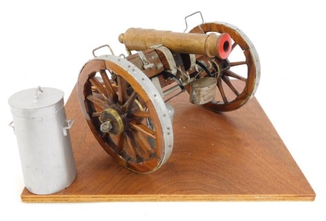 A model cannon, on wooden plinth base, with silver painted spiked wheels, and gold painted barrel, 14cm high, the base 25cm x 25cm.