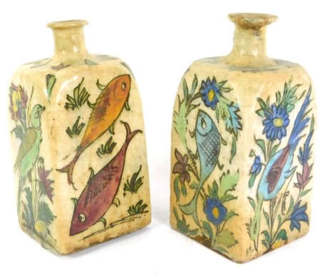 A pair of Persian Iznik Qajar pottery bottles, each on a cream glazed ground, depicting birds and flowers, 21cm high. (AF)