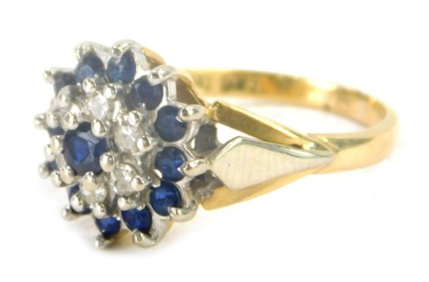 An 18ct gold sapphire and diamond cluster ring, the central stone sapphire surrounded by halo of diamonds and further surrounded by sapphires, with bicolour V splayed shoulders, ring size M, 4.7g all in.