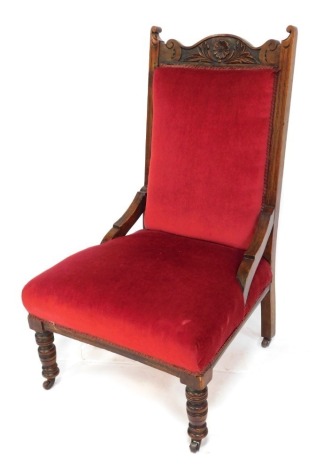 A Victorian mahogany nursing chair, with a floral and foliate carved crest rail, over stuffed back and seat in red draylon, raised on turned legs, on castors, 58cm wide.