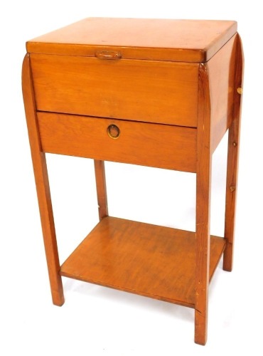 A mid century pine sewing table, the hinged lid opening to reveal a green silk lined interior, over a drop flap, enclosing two frieze drawers, all containing sewing accoutrements, raised on square legs united by an under tier, 66cm high, 39cm wide, 30cm d