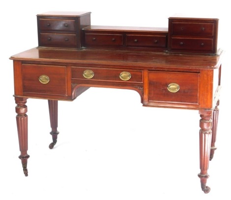 An early Victorian mahogany writing table, the raised back with an arrangement of six drawers, each with turned wood handles, the base with a moulded edge above three drawers around an arched kneehole, on turned reeded legs with brass castors, 98cm high, 