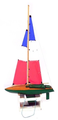 A radio controlled wooden model of a yacht, with a green and wooden planked hull, fully rigged sale, on a wooden stand, 110cm wide.