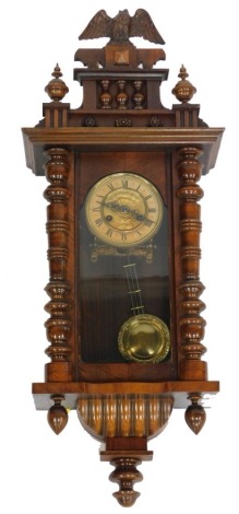 A late 19thC American oak cased wall clock, circular brass dial embossed with flowers, chapter ring bearing Roman numerals, eight day movement, the case with a shaped pediment with eagle and turned finial surmount, glazed front with turned pilasters, rai