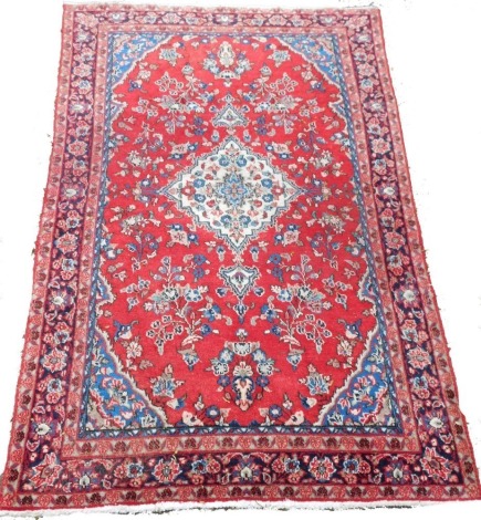 A Kashan red ground rug, the central diamond decorated with flowers, against a floral ground within floral borders, 203cm x 124cm.