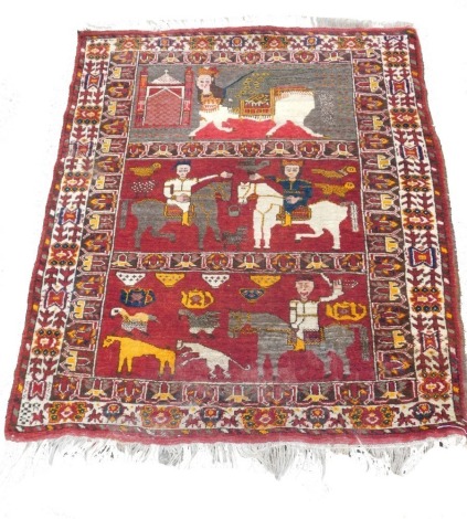 A Persian Shiraz figural red ground rug, the upper panel with a winged and figural horse and mask, central panel with figures on horseback and birds, the lower panel with a figure on horseback and birds and animals, within repeating floral and geometric b