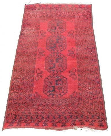 An Afghan red ground rug, with four central medallions, within repeating geometric borders, 191cm x 102cm.