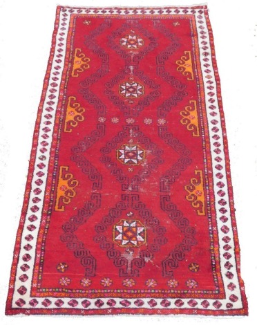 A Caucasian Nomadic red ground rug, decorated with four central medallions, floral and foliate motifs, within a repeating floral border, 194cm x 101cm.