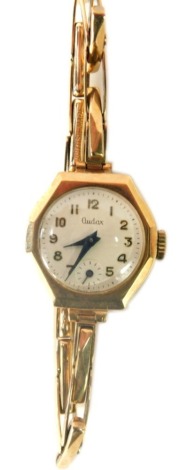 An Audax 9ct gold cased lady's wristwatch, with an octagonal watch head, with a cream coloured dial with blue hands, on expanding 9ct gold bracelet, 2cm wide, 16g all in, boxed.