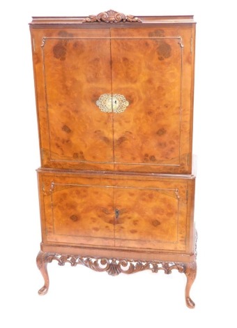 A 20thC walnut cocktail cabinet, with scroll carving above two doors with elaborate escutcheons, revealing a fitted interior above double cupboards, on cabriole legs, with key, 169cm high, 90cm wide, 46cm deep.