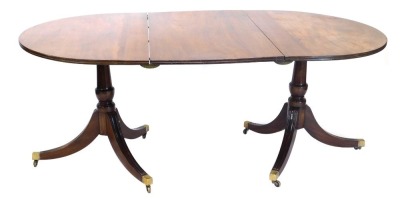 A mahogany twin pedestal extending dining table, the D end top on twin pedestal baluster stems, each terminating in triple sabre legs with brass caps and castors, with one leaf, 71cm high, 172cm wide, 100cm deep.