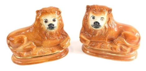 A pair of Staffordshire style pottery figures of recumbent lions, each in brown with gilt highlights, 22cm high. (2, AF)