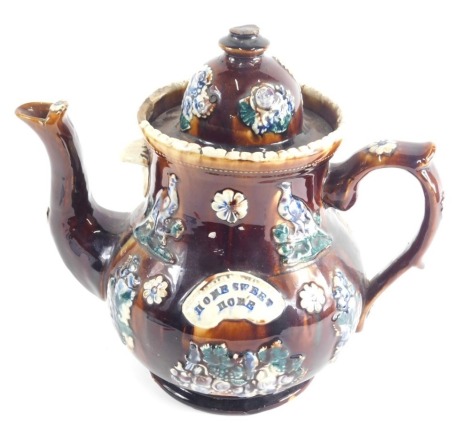 A Bargeware treacle glazed pottery teapot, with domed lid, thumb mould handle and shaped body with rosettes and flowers, marked Home Sweet Home, 29cm high (AF)