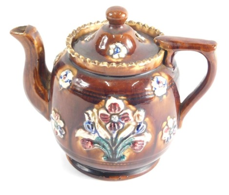 A Bargeware treacle glazed pottery teapot, raised with flowers on circular foot, 15cm high.