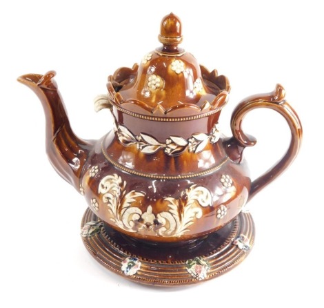 A Bargeware treacle glazed pottery teapot on stand, with acorn knop, moulded spout, thumb mould handle, and circular stand, raised with flowers, unmarked, 38cm high.