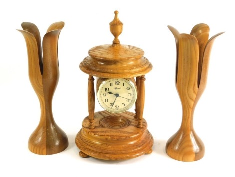 A lightwood Hermle quartz clock garniture, comprising clock with 8cm diameter Arabic dial, suspended on turned pillars, on a circular foot, with two similar vase garniture. (3)