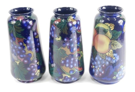 Three similar Royal Stanley Jacobean vases, each typically decorated in opalescent pattern with fruit, grapes, etc., on a blue ground, 27cm high. (3)