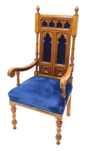 A Victorian gothic oak throne chair, with acorn finials, upholstered back and seat in blue velvet, on turned front legs with heavy scroll arms and Gothic style back panels, 118cm high.