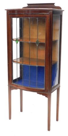 An Edwardian mahogany display cabinet, the bowfront with astragal glazed lead panelled doors inset with green glass sections, on square tapering legs, with a boxwood inlay, 146cm high, 64cm wide, 35cm deep.