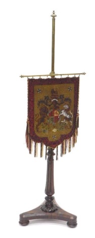 A 19thC rosewood pole screen, the brass cylindrical top with a later embroidered lion and unicorn petit point crest, on an acanthus stem terminating in a tricorn base, above compressed circular feet, 145cm high.