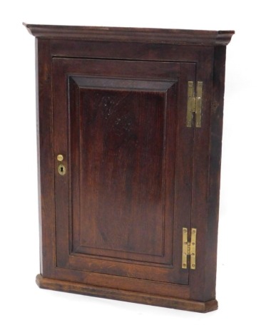 An early 18thC oak hanging corner cupboard, with a fixed cornice above a fielded panelled door revealing fixed shelves with a plain moulded base, 94cm high, 65cm wide, 46cm deep.