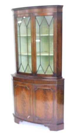 A late 20thC mahogany freestanding corner cabinet, the dentil top raised above a pair of astragal glazed doors revealing fixed shelves, above a double cupboard with panel doors, on bracket feet, 179cm high, 91cm wide, 64cm deep.