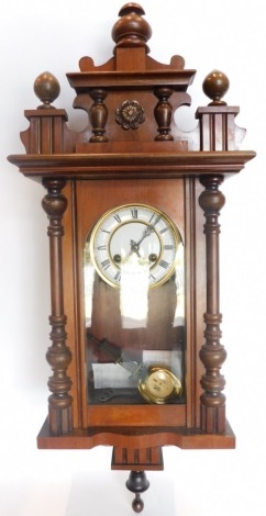 An early 20thC walnut Vienna wall clock, the 12cm diameter Roman numeric dial, in a three part glazed case flanked by quarter columns and surmounted by a carved cornice with rosette patera, flanked by shaped finials, with an eight day movement, with pendu