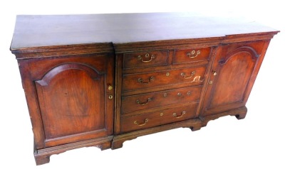 An early 19thC oak breakfront dresser base, with an arrangement of two short and three long drawers with drop handles to the centre, flanked by two cupboards with arched panels, on bracket feet, 68cm high, 185cm wide, 60cm deep.
