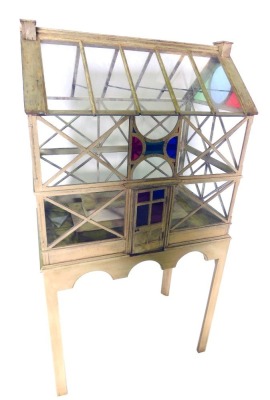 A painted and glazed terrarium, modelled in the form of a 19thC glass house, with stained glass to the gables, plain astragals, on a rectangular stand with arched apron, on chamfered legs, 82cm wide, 51cm deep, 155cm high.