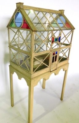 A painted and glazed terrarium, modelled in the form of a 19thC glass house, with stained glass to the gables, plain astragals, on a rectangular stand with arched apron, on chamfered legs, 82cm wide, 51cm deep, 155cm high. - 2