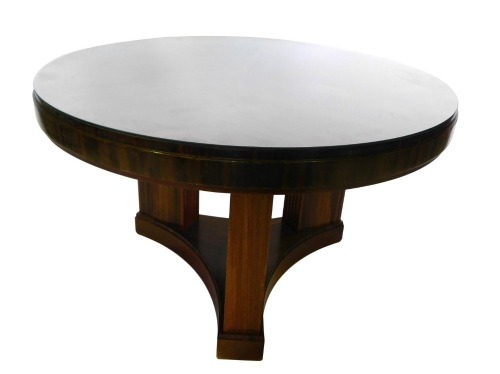 An Art Deco mahogany and calamander display table, with a circular glazed top, on four square section supports with concave platform and plinth, 123cm diameter.