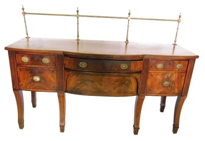 A Regency mahogany and ebony strung sideboard, with a brass gallery, a reeded edge and a bow fronted centre section, above an arrangement of two frieze drawers, a deep drawer, a concealed drawer, and a further drawer, on fluted sabre legs, 130cm high, 183