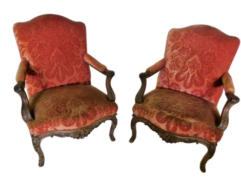 A pair of 19thC French walnut fauteuil, each with a studded coral upholstered back, padded arm rests, and seat, carved overall with scrolls, leaves, etc., on cabriole legs.