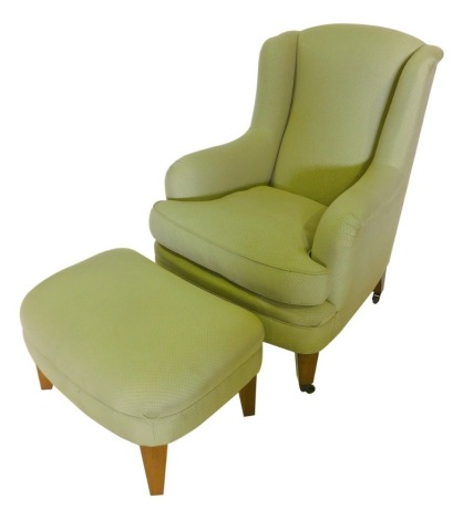 A modern wingback armchair, upholstered in green fabric, on square tapering legs with castors, and a matching footstool.