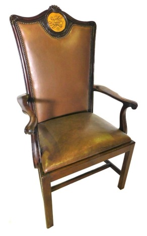 A late 19th/early 20thC mahogany throne type open armchair, the back carved with acanthus leaves, etc., with a brown leatherette padded back and seat, shaped arms, on plain supports with H stretcher, the back carved with a monogram, plaque to reverse Pres