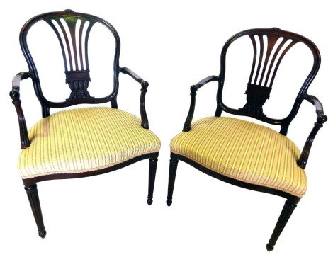 A pair of late 19thC mahogany armchairs in Sheraton style, each with a shaped back, pierced splat, and short arms carved with leaves, the padded seat upholstered in cream and green striped fabric, on turned tapering reeded legs.