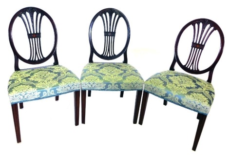 A set of three early 20thC mahogany side chairs in George III style, each with an oval back, pierced splat, and a padded seat, on square tapering legs.