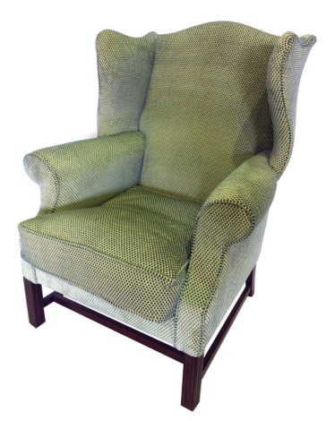 A mahogany wingback armchair in George III style, upholstered in green and cream patterned fabric, on reeded legs with H stretcher. The upholstery in this lot does not comply with the 1988 (Fire & Fire Furnishing) Regulations, unless sold to a known expo