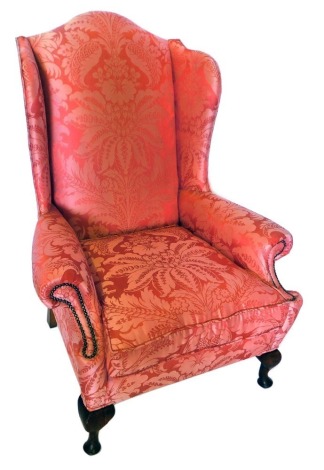 A mahogany wingback armchair in George III style, upholstered in red Damask fabric, with brass studded borders, on short cabriole legs, with pad feet.