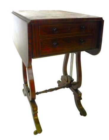 A Regency rosewood and brass inlaid drop leaf work table, the rectangular top with rounded corners, above two drawers, each with turned wood handles, on lyre shaped supports, with turned stretcher and sabre legs, terminating in cast brass castors, 73cm hi