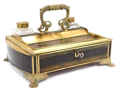 A Victorian brass and leather bound desk stand, with brass carrying handle, having two cut glass inkwells with brass circular lids, embossed with foxes heads and vines, flanking a brass lidded recess, over a frieze drawer, raised on lion paw feet, 32cm wi