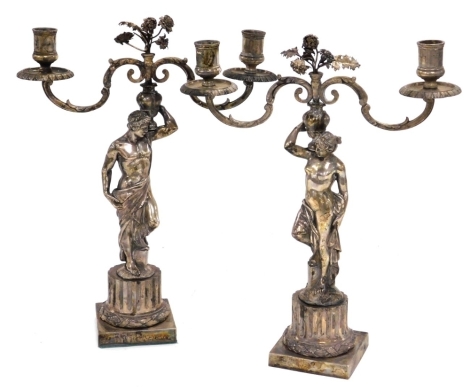 A pair of late 19thC silver plated candelabra, cast as a Roman God and Goddess, each supporting on their shoulder a vase of flowers, raised on a fluted and wreath embossed partial column above a square base, 34cm high.