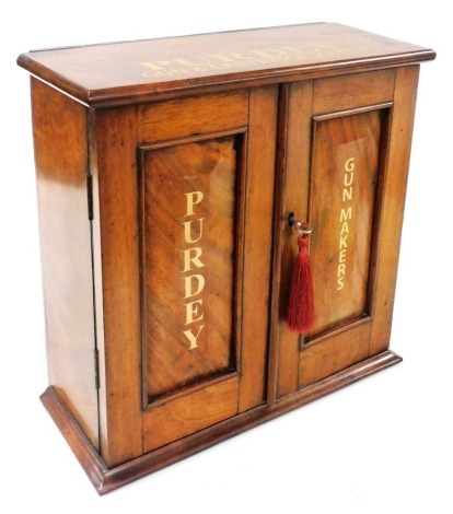 A late Victorian Purdey walnut and mahogany gun and cartridge maker's display cabinet, with two panelled doors, printed in gilt with Purdey, Gun Makers, opening to reveal a single shelf, raised on a plinth base, 37cm high, 38cm wide, 16cm deep.