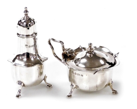 A George V silver mustard pot, with a shaped rim raised on three hoof feet, blue glass liner, together with a matching silver pepper pot, J. Sherwood & Sons, Birmingham 1918 and 1920, weighable silver 2.44oz.