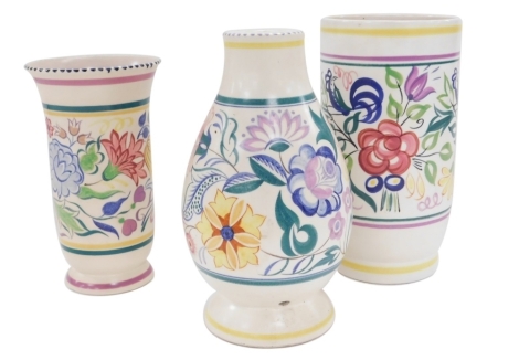 Three Poole pottery vases, each decorated with a central band decorated with flowers with further coloured banded decoration, one of cylindrical form, 25cm high, cylindrical fluted form, 21cm high, and the other of baluster form, 25cm high.