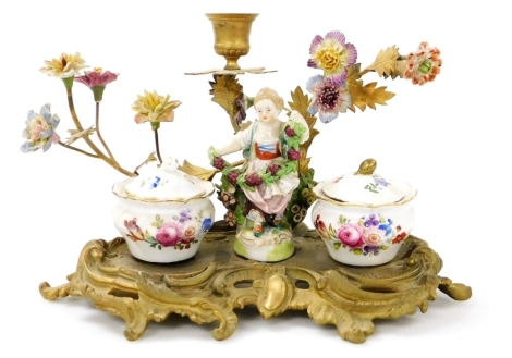 A 19thC Continental porcelain and brass desk stand, the stand surmounted by a figure of a girl holding vines, flanked by two porcelain ink pots, decorated with flowers, gilt heightened, with lids and inner ink liner, the stand with a single chamber stick 