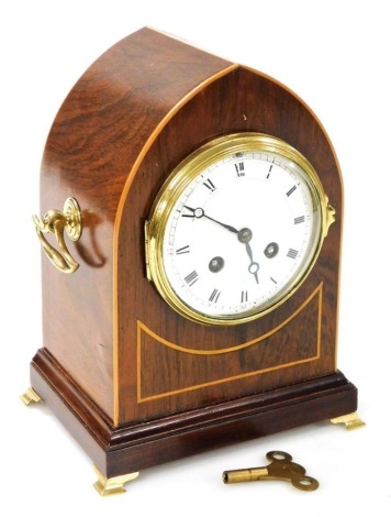 An Edwardian mahogany and boxwood inlaid mantel clock, of arched form, the Roman numeric enamel dial with eight day movement, in a case with two brass handles, raised on four brass ogee feet, with key and pendulum, 25cm high.