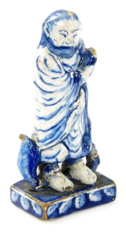 An 18thC tin glazed earthenware figure modelled as an Oriental gentleman in cloak, on a square leaf decorated base, 15cm high. (AF)