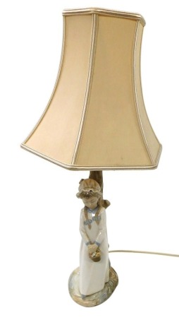 A Nao porcelain table lamp, modelled as a girl holding a basket of sweets, against a tree trunk, on a naturalistic base, with shade, 57cm high.